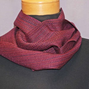 Puede incluir: Una bufanda burdeos y negra con estampado de espiga est&aacute; drapeada alrededor del cuello de un maniqu&iacute;. La bufanda est&aacute; hecha de un material suave y tejido y tiene un aspecto texturizado. Un accesorio elegante para el clima fr&iacute;o.