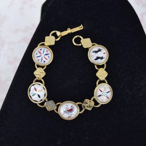 May include: Gold-toned bracelet featuring circular, patterned charms. The charms display colorful designs, including floral and bird motifs, set within a gold frame. The bracelet has a toggle clasp and geometric links.
