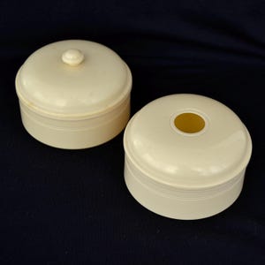May include: Two round ivory boxes with lids. One box has a small knob on the lid and the other box has a hole in the lid.