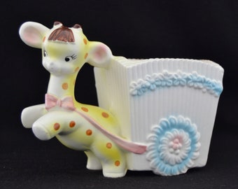 May include: A yellow and orange ceramic giraffe figurine pulling a white wagon with blue and pink floral accents. The wagon has a rectangular planter box.