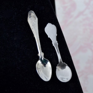 May include: Two silver teaspoons, one with a decorative handle and the other with a plain handle.