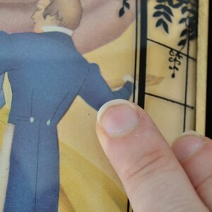 K&ouml;nnte beinhalten: Eine Nahaufnahme einer Vintage-Rahmenillustration eines tanzenden Paares. Der Mann tr&auml;gt einen blauen Anzug und die Frau ein gelbes Kleid. Der Rahmen ist mit schwarzen und goldenen Akzenten verziert.