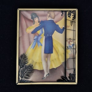K&ouml;nnte beinhalten: Eine gerahmte Illustration eines Paares, das in einem Ballsaal tanzt. Die Frau tr&auml;gt ein gelbes Kleid mit einer blauen Sch&auml;rpe und der Mann tr&auml;gt einen blauen Anzug. Der Hintergrund ist zartrosa und der Rahmen ist golden.