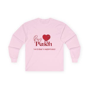 May include: A light pink long-sleeve shirt with the text "Rosy Peach" in a cursive font and a red heart graphic. Below the text is the phrase "THIS ENERGY IS IRRESPONSIBLE" in a sans-serif font.