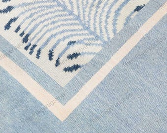 May include: A close-up of a blue and white rug with a leaf pattern. The rug has a light blue background with a white border and a light pink accent. The leaf pattern is in shades of blue.
