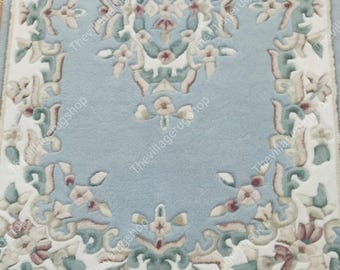 Può includere: Un tappeto rettangolare con sfondo azzurro e un intricato motivo floreale in crema, verde e rosa. Il tappeto presenta un bordo dettagliato e un design centrale, per l'arredamento della casa.