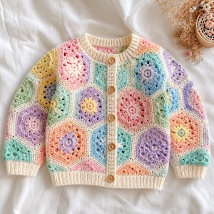May include: A long-sleeve cardigan made of multicolored crocheted hexagonal motifs in pastel shades of pink, yellow, blue, purple, and green. The garment features a cream-colored ribbed collar, cuffs, and hem, secured with five round wooden buttons.