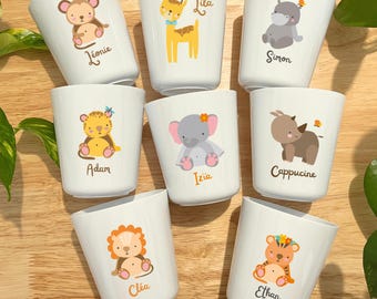 Può includere: Una collezione di tazze in ceramica bianca, ognuna decorata con un'illustrazione di animali dei cartoni animati e un nome. Gli animali includono una scimmia, una giraffa, un ippopotamo, una tigre, un elefante, un rinoceronte e un leone. I nomi sono scritti in corsivo.