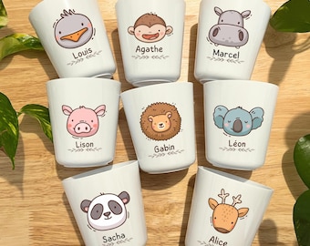 Può includere: Otto tazze in ceramica bianca, ognuna decorata con una diversa illustrazione di animali dei cartoni animati e un nome. Gli animali includono un'anatra, una scimmia, un ippopotamo, un maiale, un leone, un koala, un panda e un cervo. I nomi sono in corsivo.