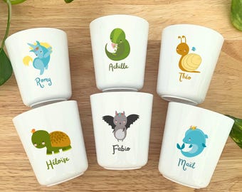Può includere: Sei tazze in ceramica bianca con illustrazioni di animali dei cartoni animati e nomi. Gli animali includono un unicorno blu, un dinosauro verde, una lumaca, una tartaruga, un pipistrello e un delfino. Ogni tazza ha un nome diverso.