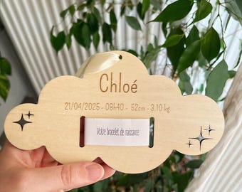 Puede incluir: Un recuerdo de madera con forma de nube con el nombre "Chloé" grabado. Incluye la fecha, hora, longitud (52cm) y peso (3,10 kg) de un recién nacido. También está presente el texto "Votre bracelet de naissance".