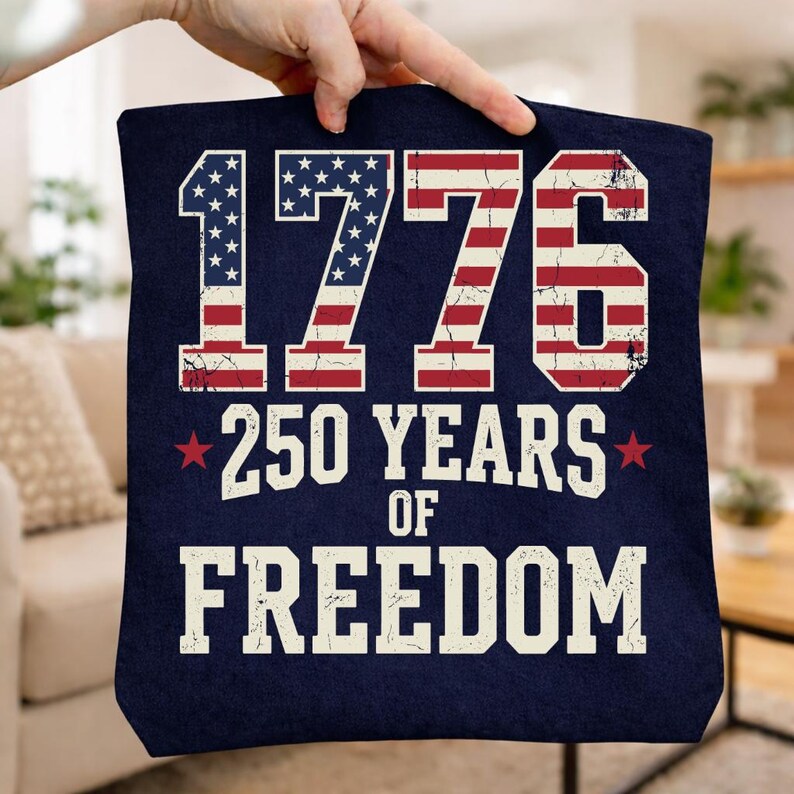 May include: A navy blue tote bag featuring the text "1776 250 YEARS OF FREEDOM" in white. The numbers and letters are designed with the American flag's stars and stripes. Red stars flank "250 YEARS".