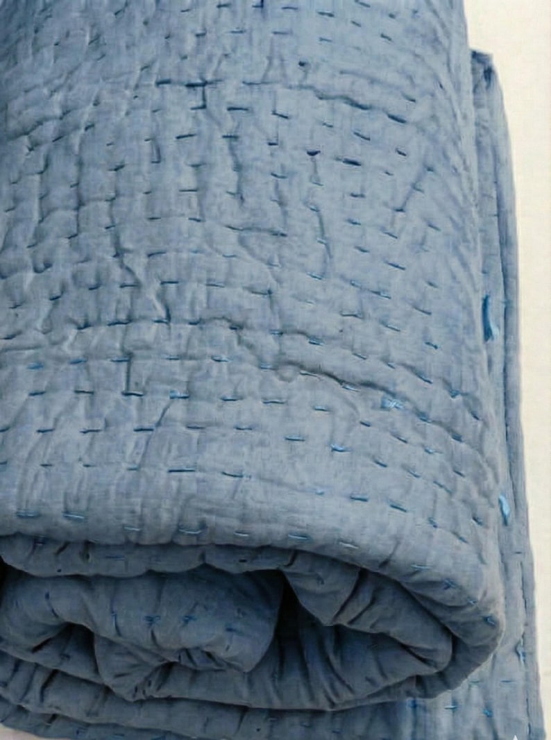 May include: A rolled-up, light blue quilt with visible stitching. The quilt is made of a soft, textured fabric and has a handmade appearance. The stitching is a darker shade of blue, creating a subtle contrast.