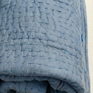 May include: A rolled-up, light blue quilt with visible stitching. The quilt appears to be made of a soft, textured fabric. The stitching is a darker shade of blue, creating a subtle contrast. The overall aesthetic is simple and cozy.