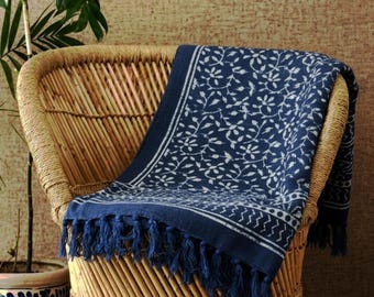 May include: A navy blue throw blanket with a white floral pattern and fringe detail is draped over a wicker chair. The blanket has a border with a white design and is made of a soft material.
