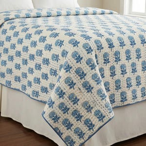 Puede incluir: Un edredón con estampado floral blanco y azul sobre una cama. El edredón presenta un patrón repetitivo de flores azules sobre un fondo blanco. Los bordes están ribeteados con un borde azul. La cama tiene una falda de cama blanca.