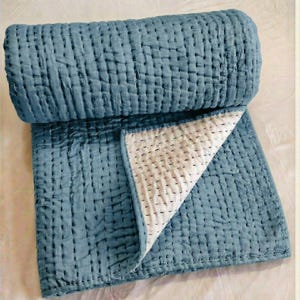 May include: A rolled-up, blue quilted blanket with a white interior. The blanket is made of a soft, textured fabric and features a grid-like stitching pattern. The corner is folded back, revealing the white interior.