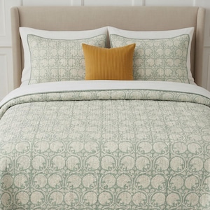 May include: A bedding set featuring a quilt and two matching pillow shams with a sage green and white circular botanical pattern. A solid mustard yellow rectangular accent pillow is centered in front of the two white-bordered pillow shams.