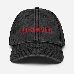 May include: A black baseball cap with the embroidered text "NO COMMENT" in red. The cap has a curved peak and a distressed appearance, suggesting a worn or retro aesthetic. The cap is a classic six-panel design, suitable for casual wear.