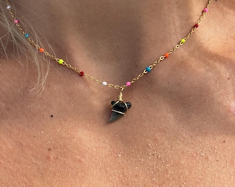 May include: Gold-toned necklace with a shark tooth pendant. The chain features colorful beads in red, orange, yellow, green, blue, and white. The shark tooth is wrapped in gold wire.