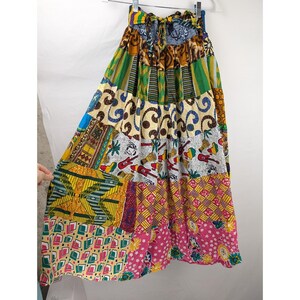 May include: A floor-length skirt featuring a patchwork design with various colorful patterns including geometric shapes, floral prints, and musical instrument motifs in shades of yellow, green, blue, pink, and white with a tie waist.