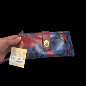May include: A leather wallet with a floral design in shades of blue and red. The wallet has a clasp closure and a zipper. The tag reads "Patricia Nash Designs".