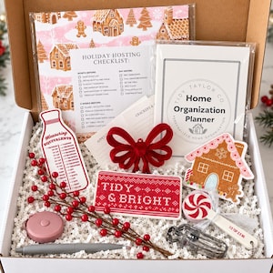 May include: A holiday gift box containing a Tidy Taylor Co. home organization planner, a holiday hosting checklist, a red velvet bow, a gingerbread house cutout, a measuring equivalents card, a red and white peppermint spoon, and a red berry sprig.