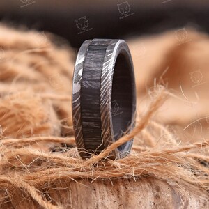 May include: A ring featuring a central band of dark, textured material flanked by two outer edges of silver-toned metal with a swirling, layered pattern. The ring has a flat profile and a smooth, polished finish on the metallic sections.
