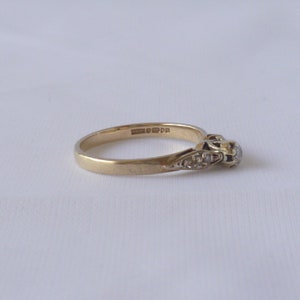 May include: A gold band ring with a single round diamond and smaller diamonds set in the band. The ring is marked "9ct 375".