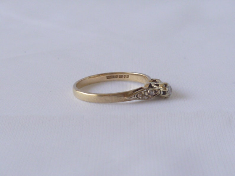 May include: A gold band ring with a single round diamond and smaller diamonds set in the band. The ring is marked "9ct 375".
