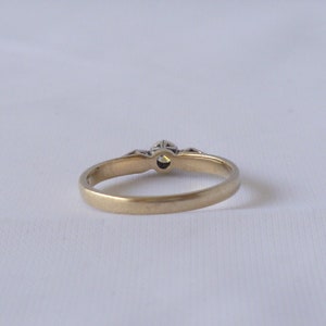 May include: A gold band ring with a single, clear gemstone in the center and smaller gemstones on either side.