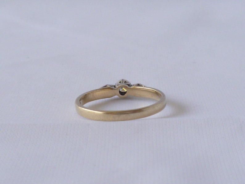 May include: A gold band ring with a single, clear gemstone in the center and smaller gemstones on either side.