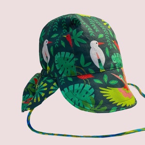 May include: A green sun hat with a tropical print featuring white birds, red and green leaves, and a yellow bird with pink accents. The hat has a wide brim and a tie.