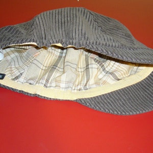 Puede incluir: Una gorra de pana marr&oacute;n con forro a cuadros y una banda el&aacute;stica amarilla. La gorra tiene una etiqueta de talla que dice "M".