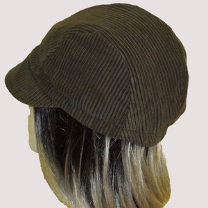 Puede incluir: Una gorra de newsboy de pana marr&oacute;n con una visera corta. La gorra est&aacute; hecha de un tejido suave y texturizado.