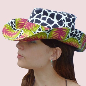May include: A wide-brimmed hat with a black and white animal print crown and a green and pink floral print brim. The hat is worn by a person with long brown hair.