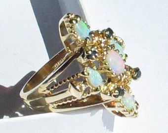 May include: A gold ring with a cluster of white opals and black gemstones. The ring is set in a delicate, floral design.