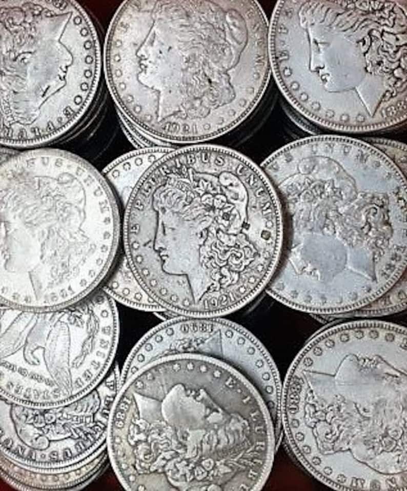 Pu&ograve; includere: Una collezione di dollari d'argento Morgan e Peace, con il profilo di Lady Liberty su ogni moneta. Le monete sono disposte in una griglia, con alcune impilate l'una sull'altra.