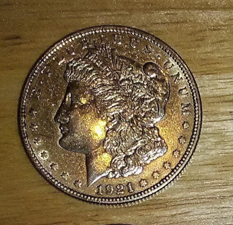 Pu&ograve; includere: Una moneta d'argento americana Peace Dollar con l'anno 1921 inciso sul fondo. La moneta presenta un profilo di una donna con i capelli fluenti e le parole "LIBERTY" e "E PLURIBUS UNUM" in alto.