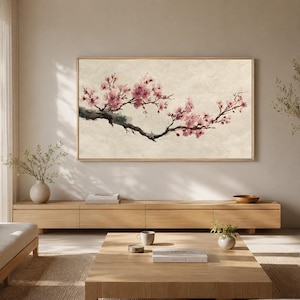 Peut inclure: Une œuvre d'art murale rectangulaire représentant une branche d'arbre horizontale avec des fleurs de cerisier roses, peinte dans un style aquarelle doux sur un fond beige texturé, encadrée par un cadre en bois clair fin.