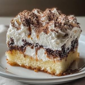 Könnte beinhalten: Ein Stück mehrschichtiger Kuchen auf einem weißen Teller. Der Kuchen hat eine gelbe Biskuitbasis, eine dunkle Schokoladenfüllung und eine dicke Schicht Schlagsahne, bestäubt mit Kakaopulver. Es ist ein Dessert.