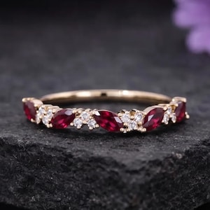 May include: A gold ring featuring a series of alternating marquise-cut deep red rubies and small round clear white stones set along the band. The design displays a repeating pattern of gemstones arranged horizontally across the top of the ring.