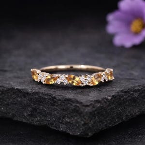 Può includere: Un anello in oro rosa caratterizzato da una serie di pietre preziose citrino giallo taglio marquise alternate a piccoli diamanti bianchi rotondi. Le pietre sono incastonate in una fila continua lungo la metà superiore dell'anello in metallo.