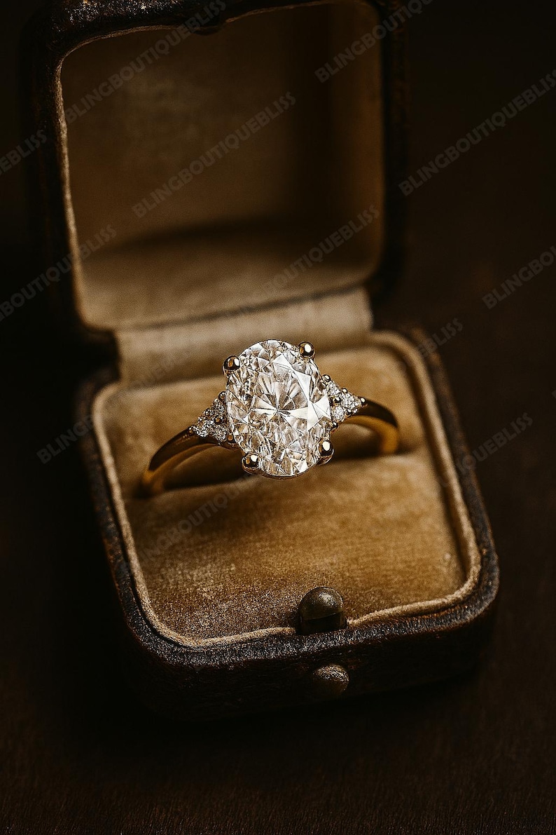 May include: A gold ring with a large oval-cut diamond center stone and smaller accent diamonds on each side. The ring is displayed in a vintage brown velvet ring box, creating a luxurious presentation.