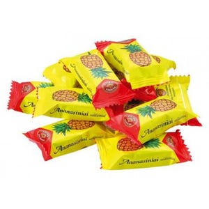 May include: A pile of individually wrapped candies. Each candy wrapper is yellow with a red top and features a pineapple illustration and the text "Ananasiniai".