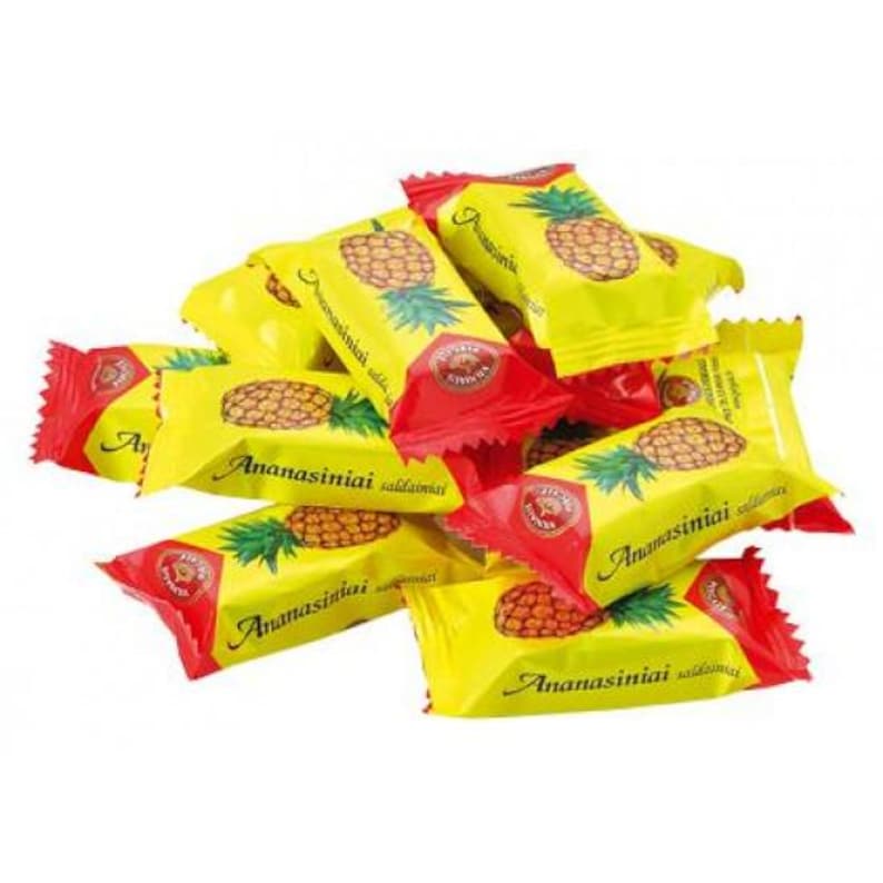 May include: A pile of individually wrapped candies. Each candy wrapper is yellow with a red top and features a pineapple illustration and the text "Ananasiniai".