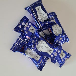 May include: A pile of individually wrapped candies with a blue and white design. Each wrapper features a white polar bear illustration and snowflake accents. The candies are arranged on a white surface.