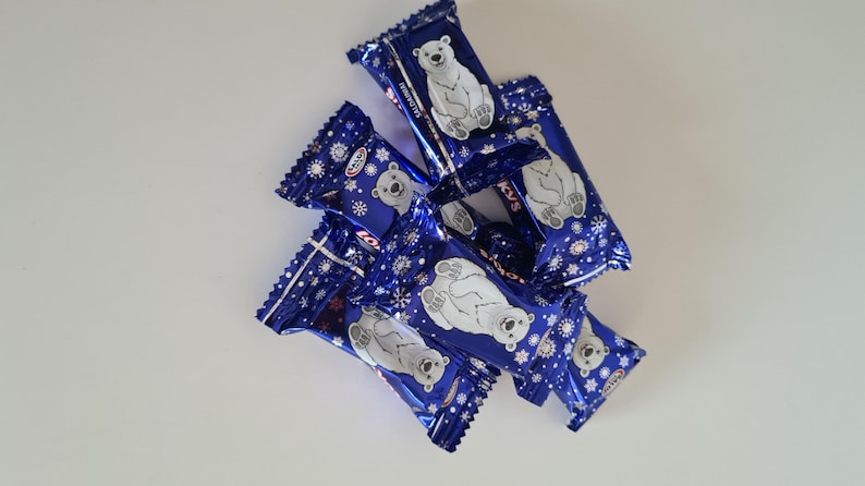 May include: A pile of individually wrapped candies with a blue and white design. Each wrapper features a white polar bear illustration and snowflake accents. The candies are arranged on a white surface.