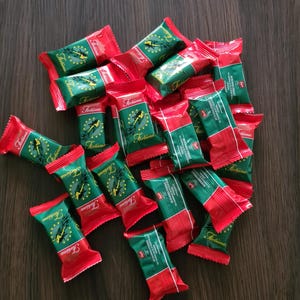 May include: A collection of individually wrapped candies with red and green packaging. The wrappers feature the word "Fortuna" in a script font, along with a graphic of a woman. The candies are scattered on a dark wooden surface.