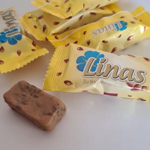 May include: Several individually wrapped candy bars with a light yellow wrapper and the word "Linas" in a stylized font. The wrappers have a floral design and scattered brown seeds. One unwrapped candy bar is visible.